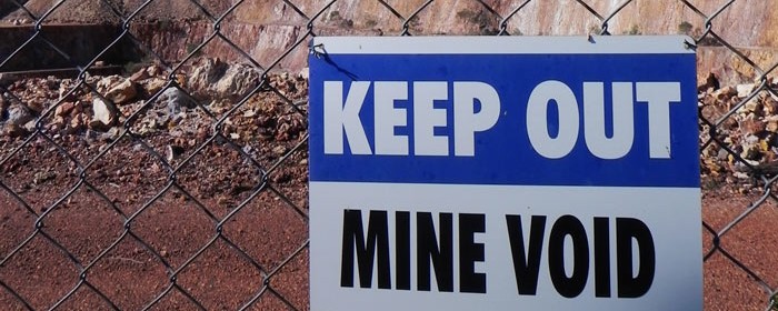 A sign attached to a fence of a mine reads 'Keep Out, Mine Void'