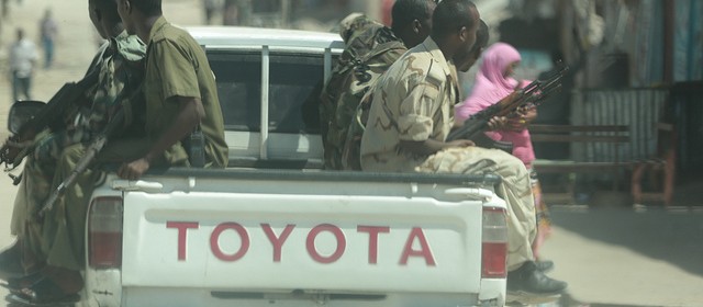 A pickup drives through Somalia's capital city, Mogadishu, with 6 armed men on the back.